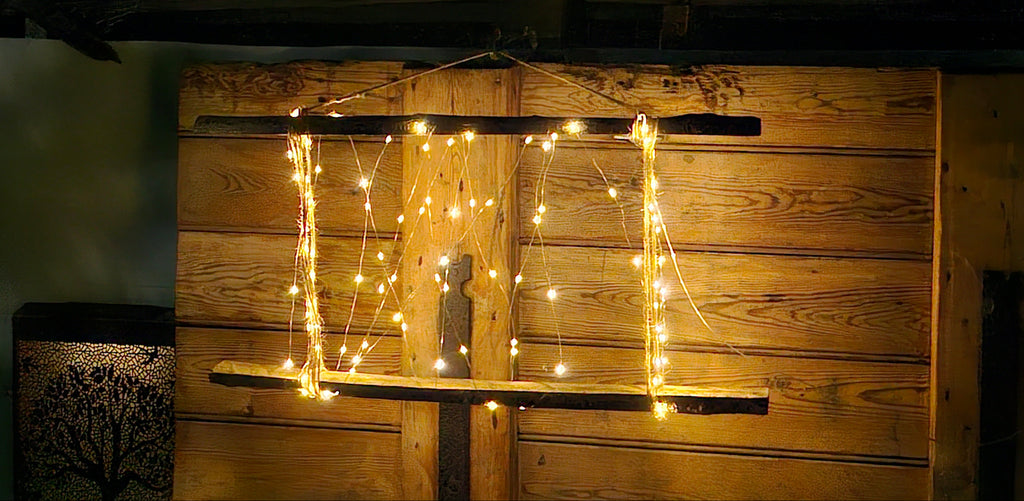 Warm white string fairy lights draped over a rustic wooden wall panel in a dimly lit interior setting.
