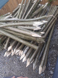 A large pile of freshly cut hazel or willow branches with pointed light wood ends, stacked outdoors on gravel next to a wooden fence.