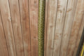 A close-up vertical shot of a slender brown hazel rod with textured bark, set against a blurred wooden fence background.
